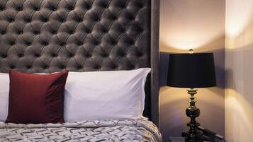 A neatly made bed with a tufted headboard, a red and white pillow, and a lamp on a bedside table.