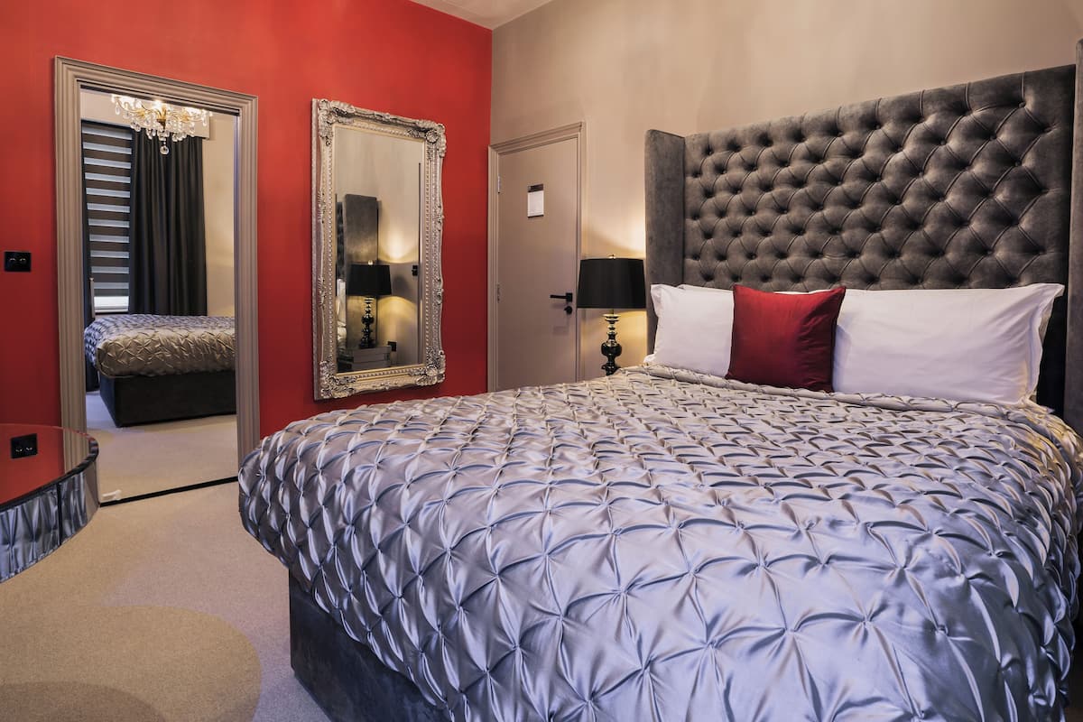 A neatly arranged bedroom with a large bed, a mirror, and a bedside table.