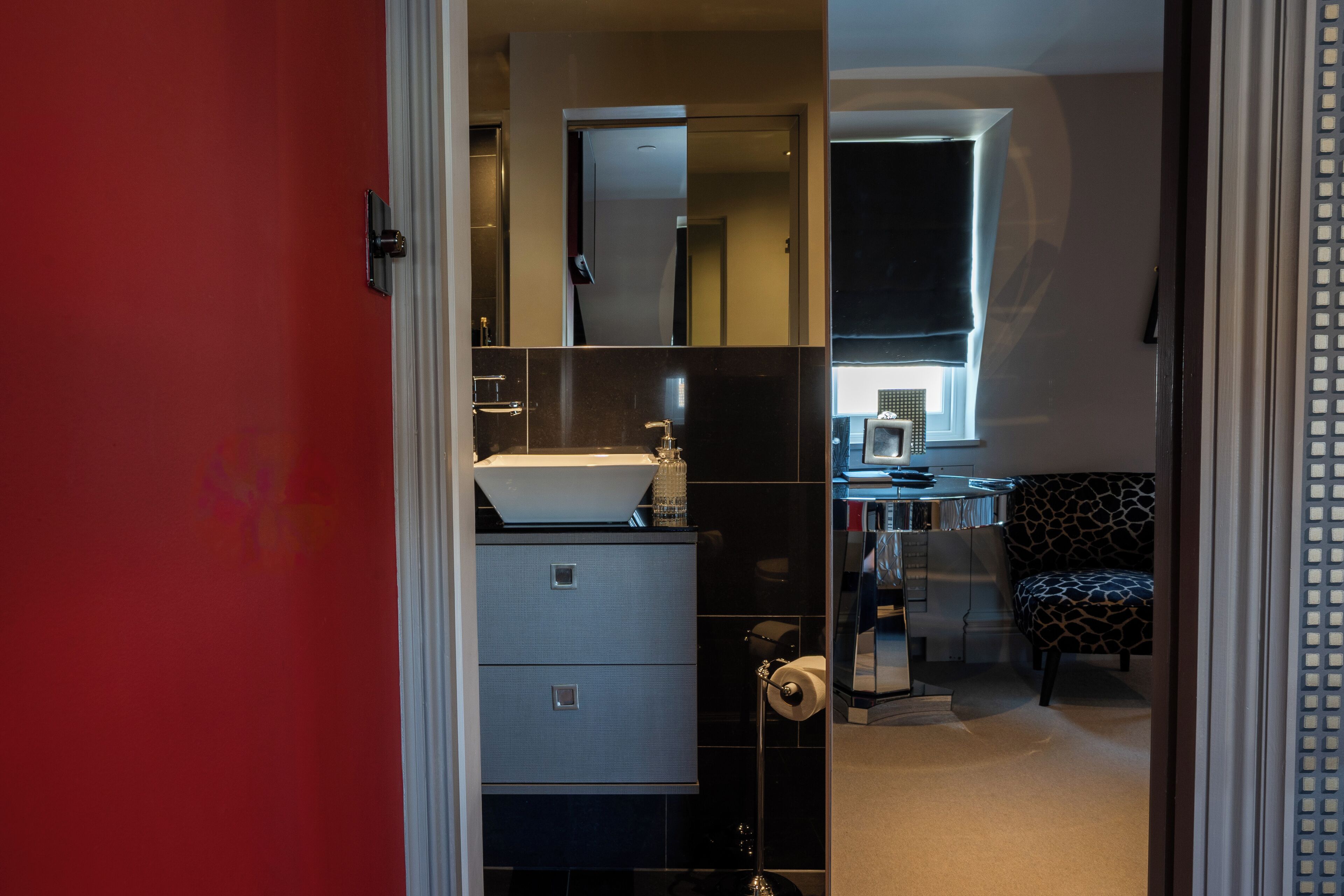 Een moderne badkamer met een witte wastafel, zwarte tegels en een spiegel erboven.
