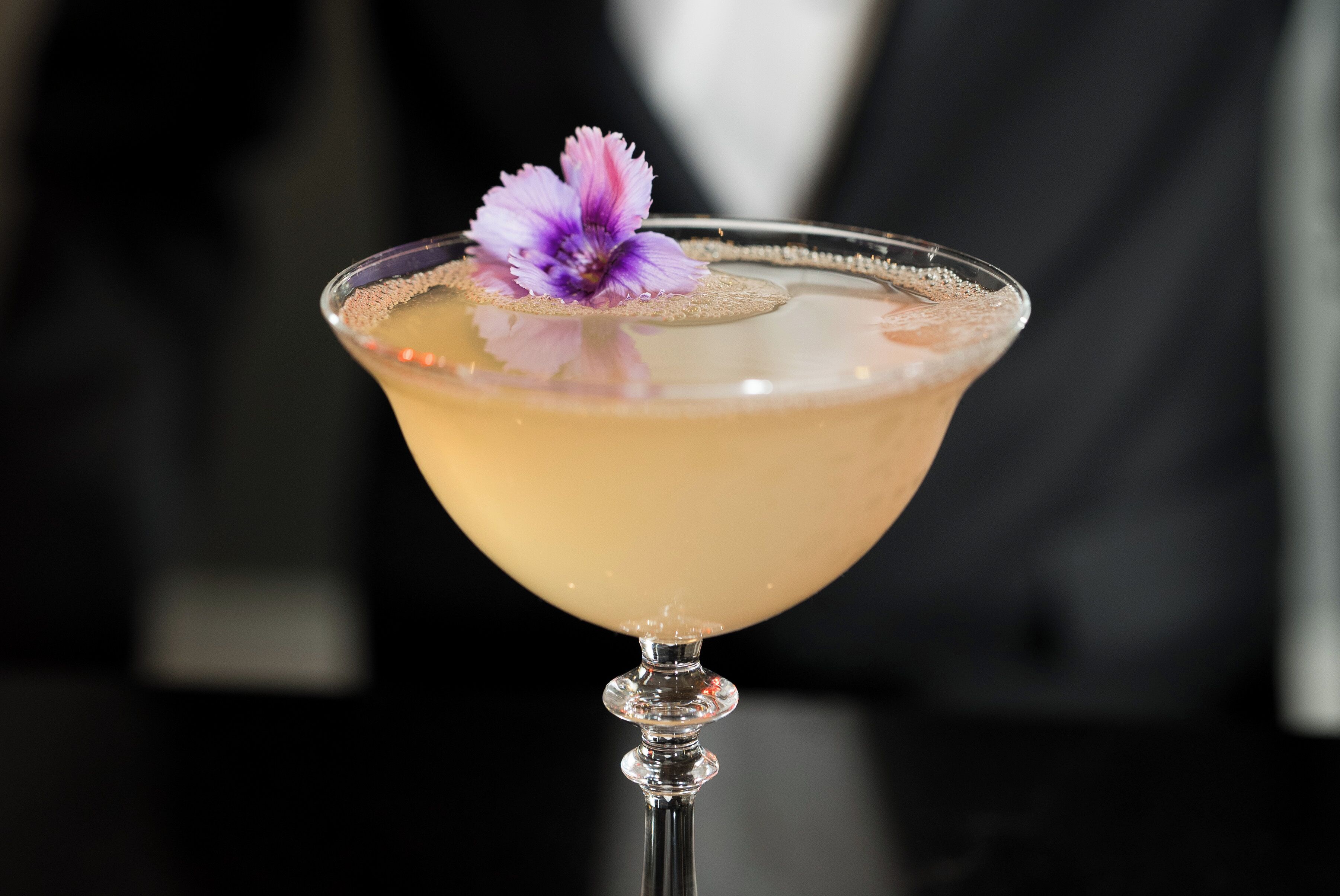 Ein Martini-Glas mit einer violetten Blütenverzierung auf einer spiegelnden Oberfläche.