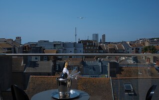 Una terraza en la azotea con una mesa y sillas, con vistas a un paisaje urbano con edificios y cielo despejado.
