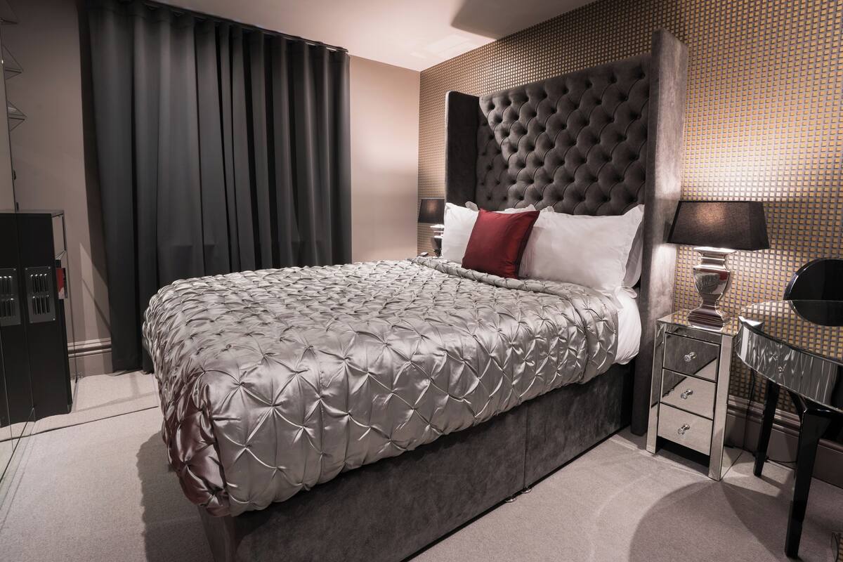 A modern hotel room with a large bed, a headboard, a nightstand, and a wall-mounted TV.