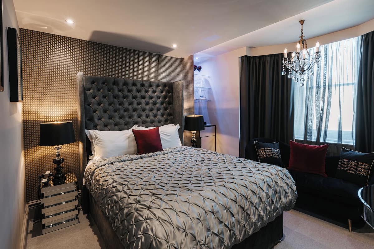 A modern hotel room with a large bed, a chandelier, and a view of the city through the window.