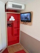 Una habitación con un armario rojo, televisor montado y aire acondicionado.