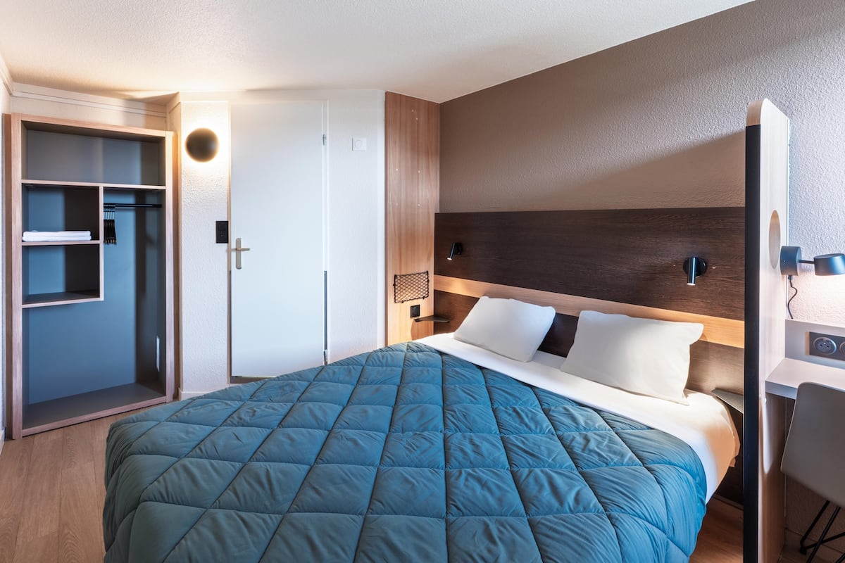 A modern hotel room with a large bed, a desk, and a wardrobe.