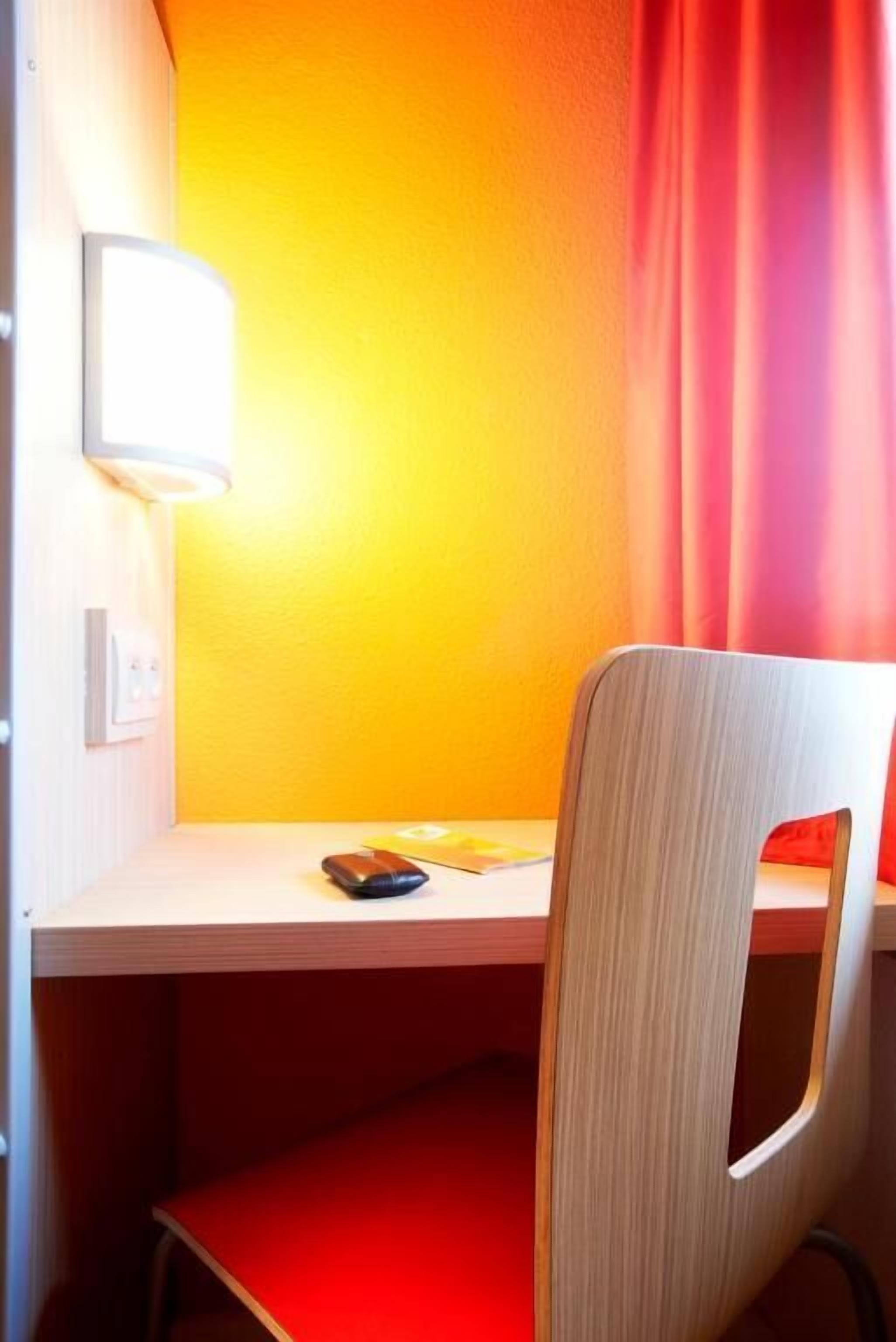 A room with a wooden desk, a red chair, and a bright yellow wall.