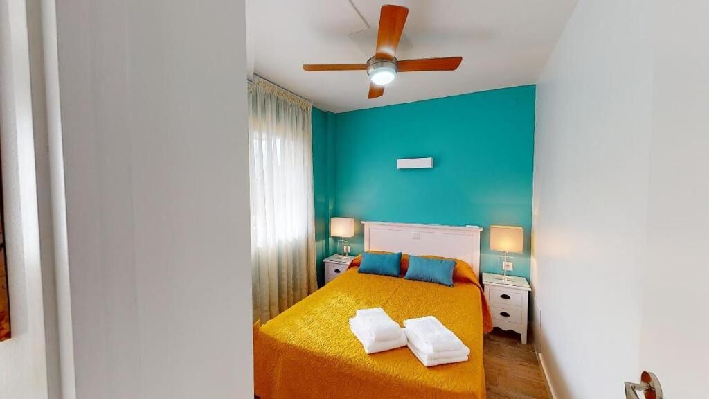 A bedroom with a bed, two bedside tables, a ceiling fan, and a window with curtains.