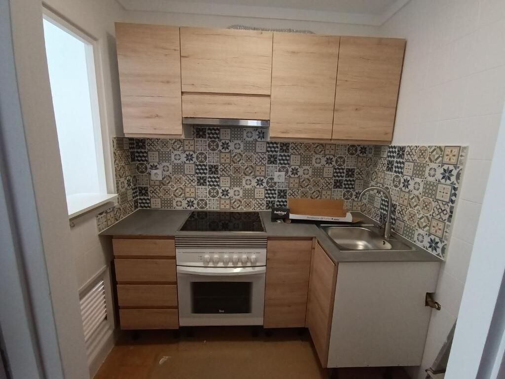 Una cocina compacta con armarios de madera, salpicadero de azulejos, horno empotrado y un lavabo.
