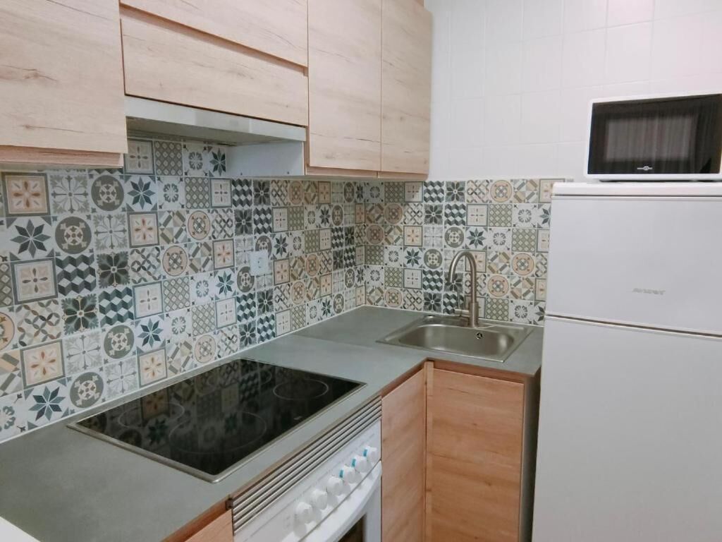 A kitchen with patterned tiles, a stove, a sink, and a microwave.