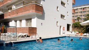 A swimming pool adjacent to a building with a brick facade and white walls, surrounded by lounge chairs and umbrellas. - Eldorado Apartamentos Turisticos (Lloret de Mar)