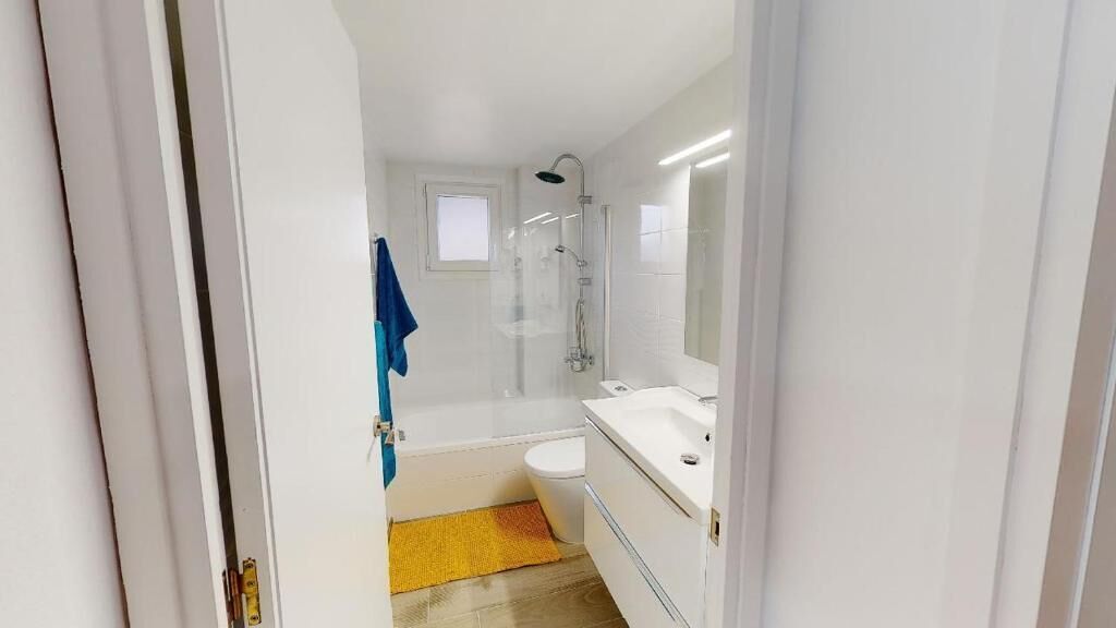 A modern bathroom with a glass shower enclosure, a white sink, and a small window.