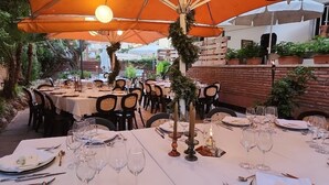 An outdoor dining area with tables set for a meal, surrounded by orange umbrellas and greenery. - Eldorado Apartamentos Turisticos (Lloret de Mar)