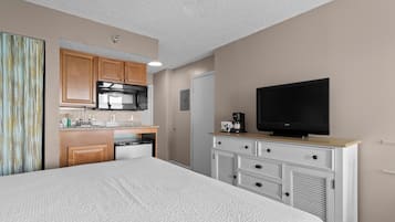 A hotel room with a bed, a television, a kitchenette, and a dresser.