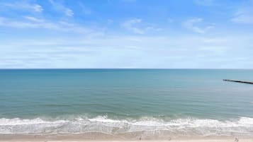 A beach with a pier extending into the water, sandy shore, and a clear sky.