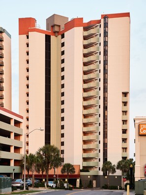 A high-rise building with multiple balconies, a parking garage, and palm trees. - The Strand - A Boutique Resort (Myrtle Beach)