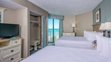 A hotel room with two beds, a television, a desk with a lamp, and a view of the ocean.