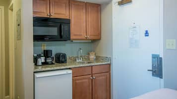 Cocina compacta con armarios de madera, microondas, cafetera y tostadora.