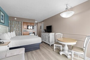 A hotel room with a bed, bedside table, chair, desk, dining table, TV, and kitchenette.