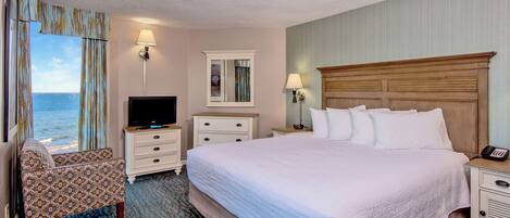 Habitación de hotel con cama, televisión, escritorio, silla y vista al océano.