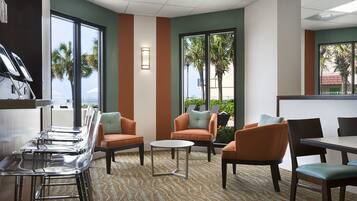 A hotel lobby with a bar area, seating, and large windows offering views of palm trees.