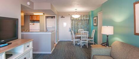 Una habitación de hotel compacta con kitchenette, comedor, sofá y televisor.