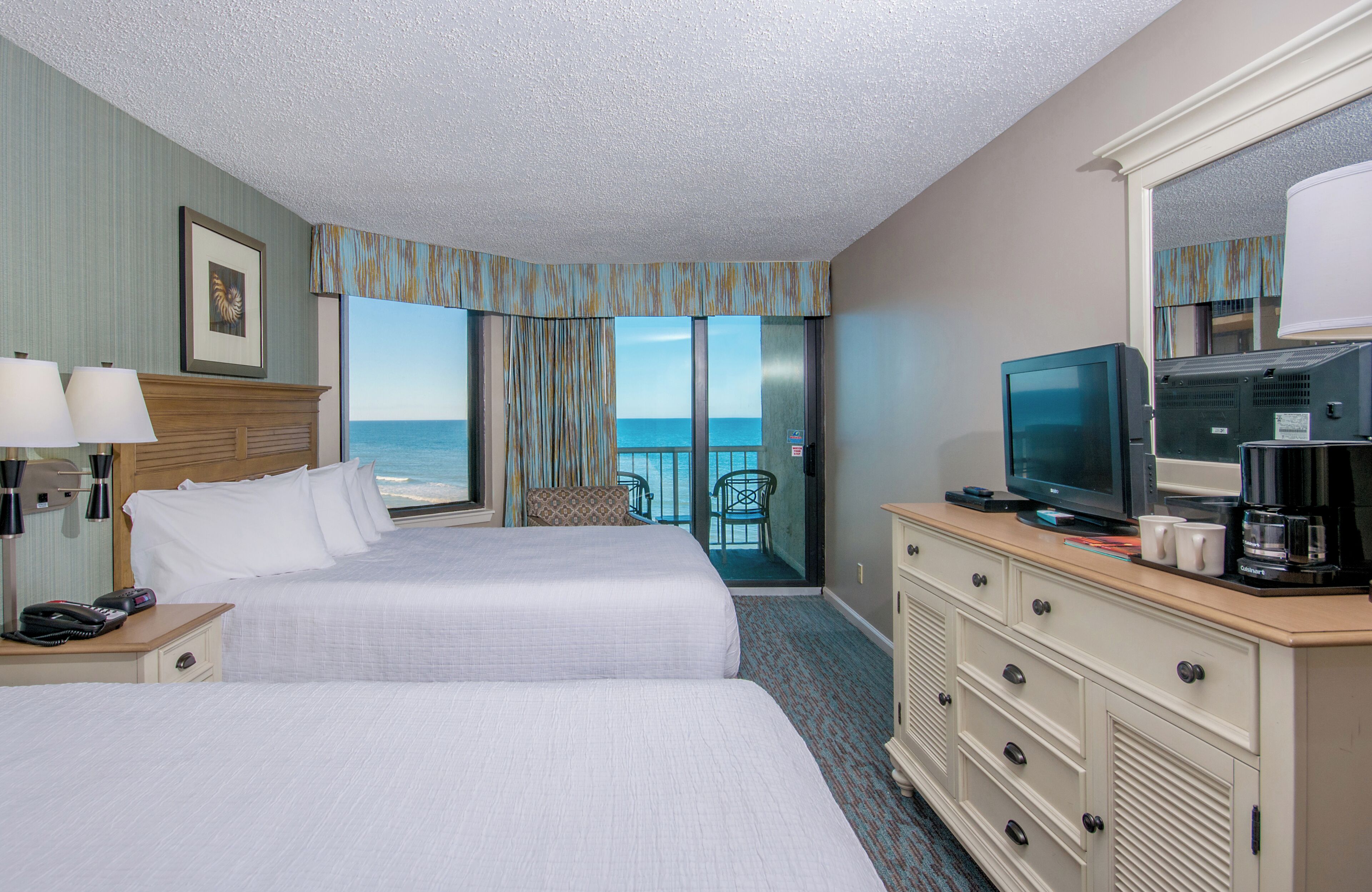 A hotel room with two beds, a television, a coffee maker, and a view of the ocean.