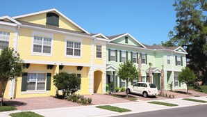 A row of three-story townhouses with a 'For Lease' sign, a car parked in the driveway, and a clear blue sky. - Coral Cay Resort by Sky Hotels & Resorts (Kissimmee)