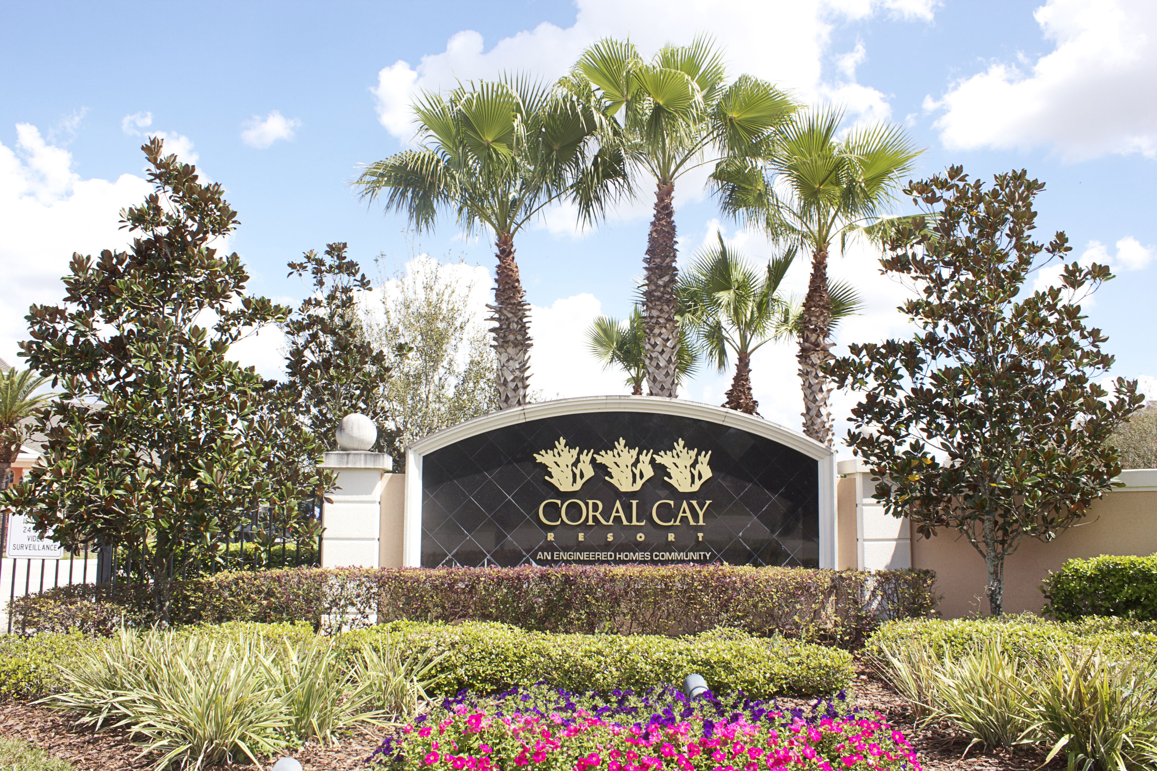 The entrance sign of Coral Cay Resort with palm trees and landscaped gardens.