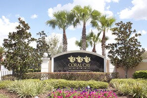 The entrance sign of Coral Cay Resort with palm trees and landscaped gardens. - Coral Cay Resort by Sky Hotels & Resorts (Kissimmee)