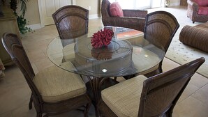 A round glass table surrounded by wicker chairs with cushioned seats. - Coral Cay Resort by Sky Hotels & Resorts (Kissimmee)