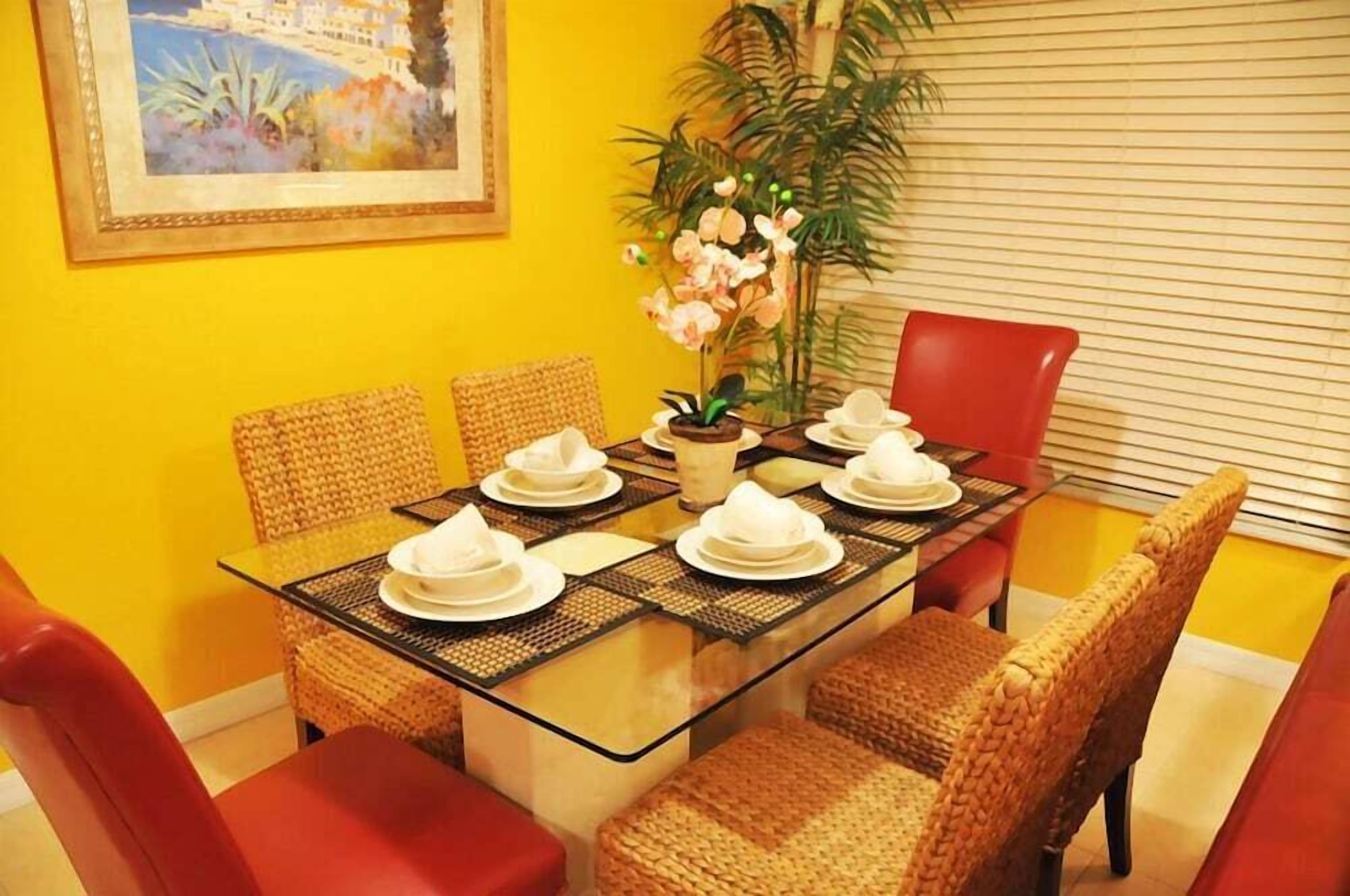 A dining area with a glass table, wicker chairs, and a potted plant.
