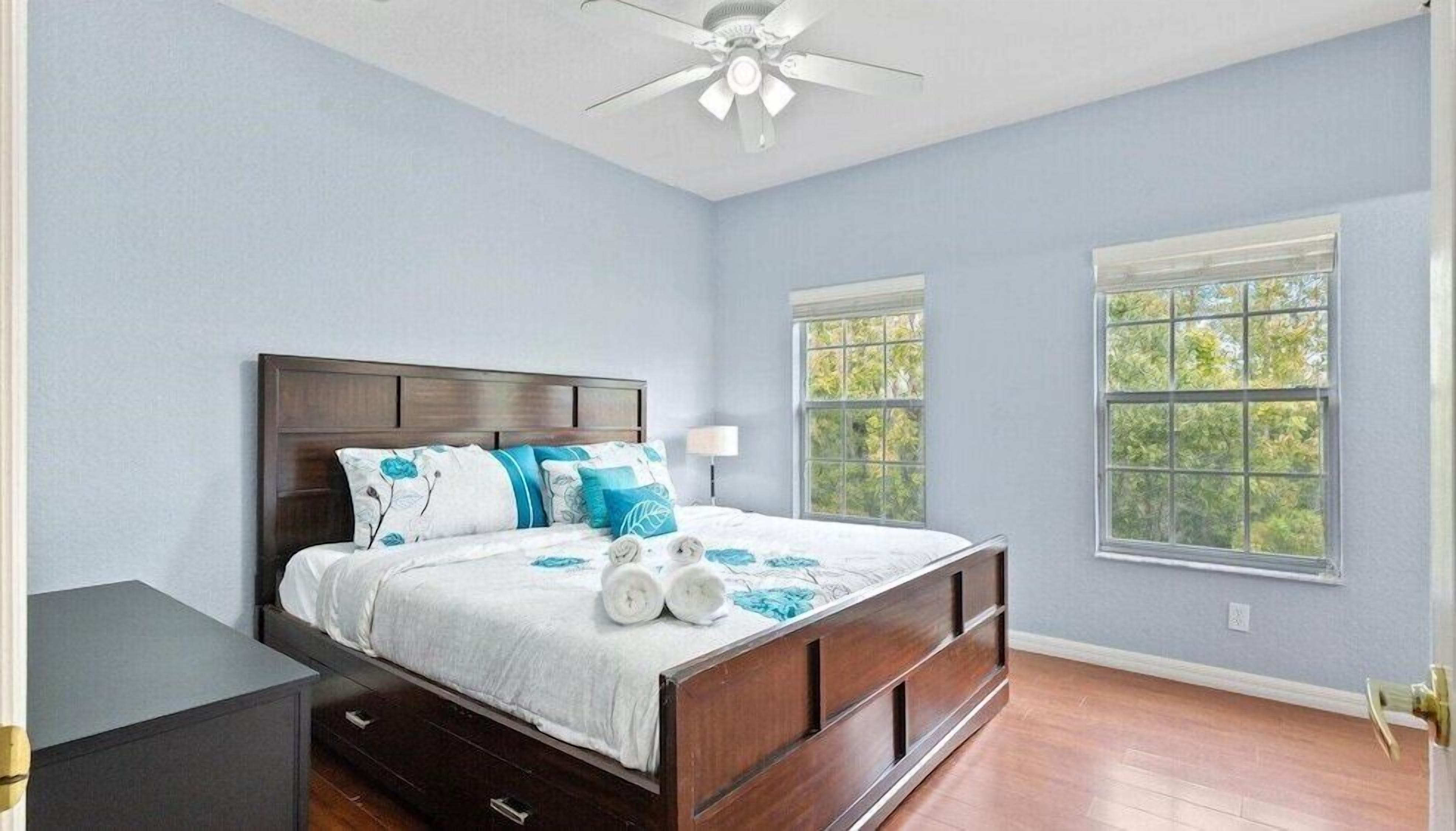 A bedroom with a wooden bed, two windows, a ceiling fan, and a nightstand.