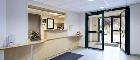 A reception area with a wooden counter, a potted plant, and a door leading outside.