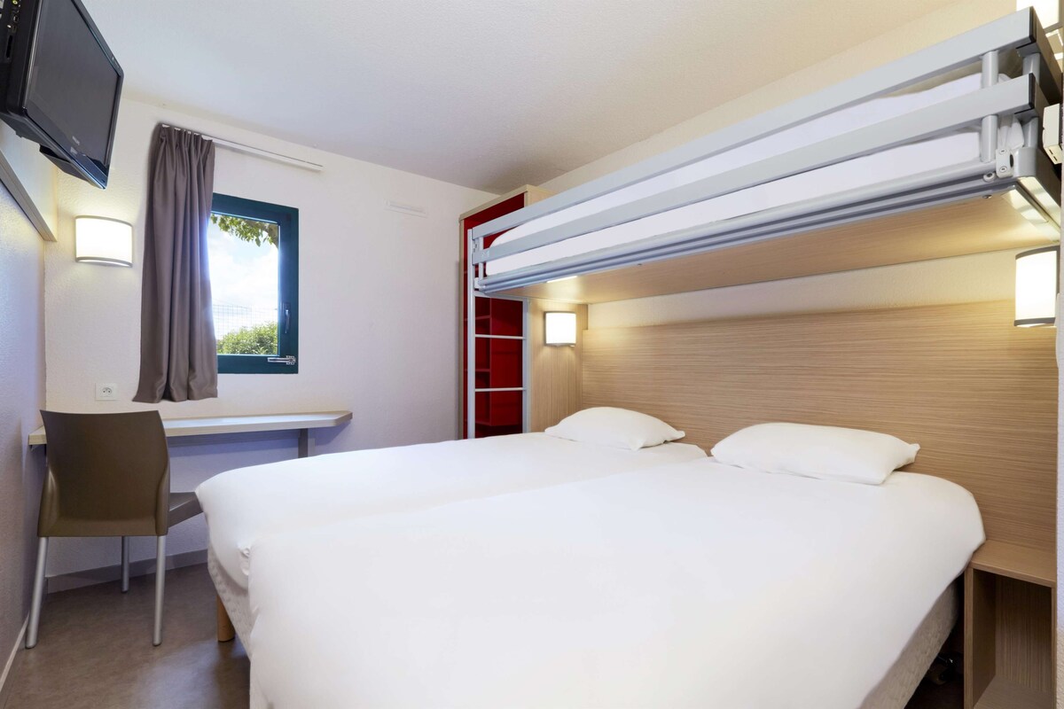 Habitación de hotel con cama, escritorio, silla, televisor y ventana con cortinas.