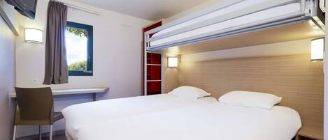 Habitación de hotel con cama, escritorio, silla, televisor y ventana con cortinas.