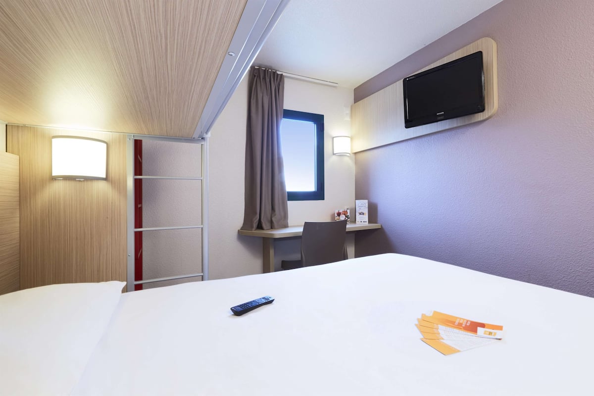 A hotel room with a bed, a desk, a TV, a window, and a curtain.