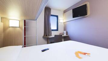 Una camera d'albergo con un letto, una scrivania, una televisione, una finestra e una tenda.
