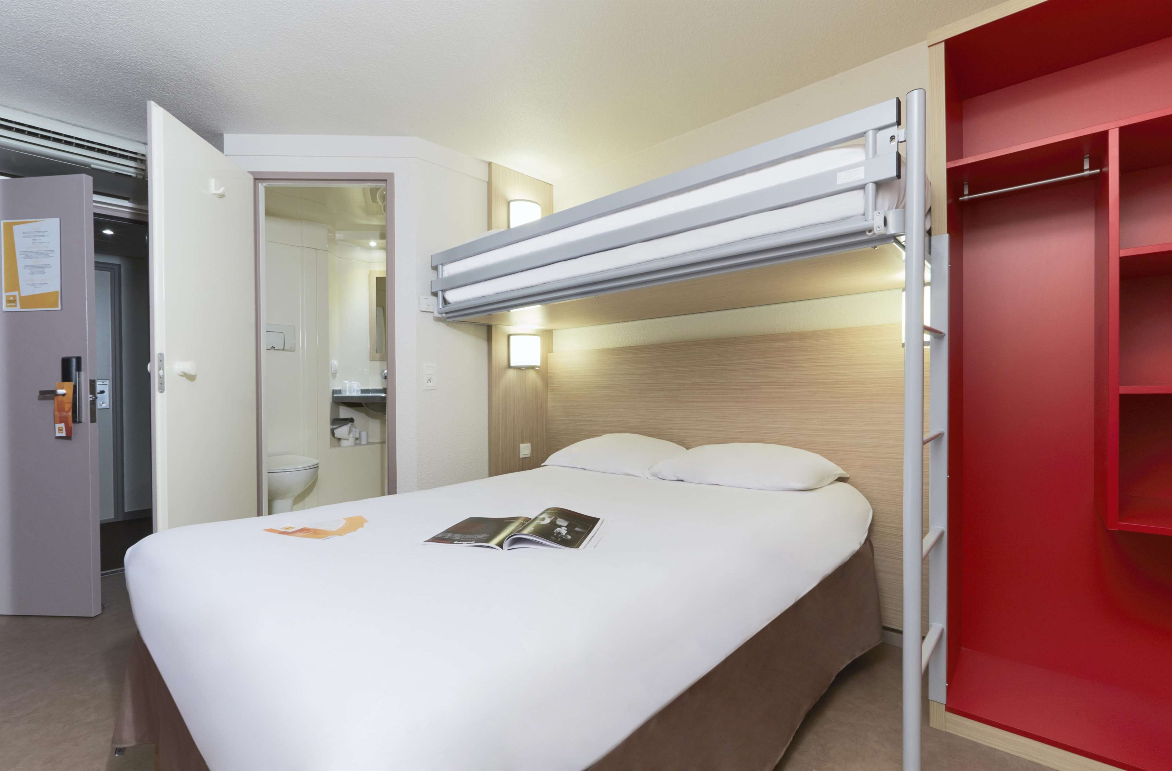A hotel room with a bed, a red wardrobe, a bathroom, and a door.