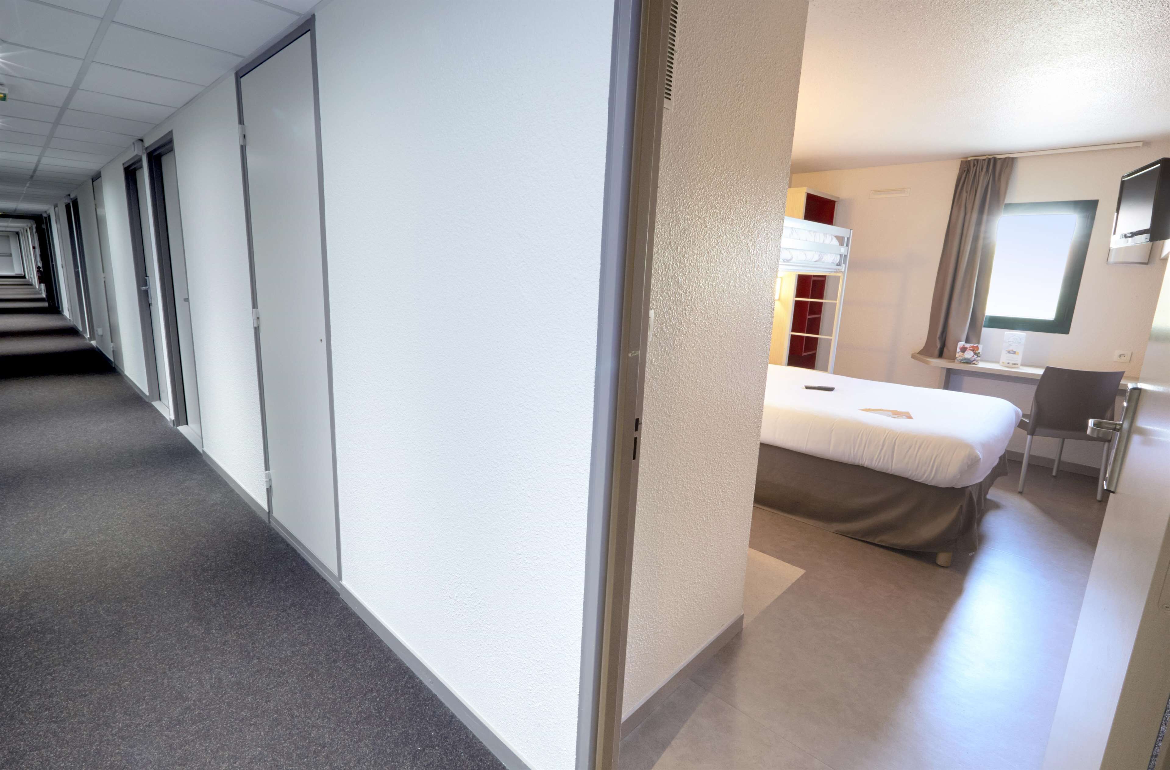 A hotel corridor with a bed, desk, and window.