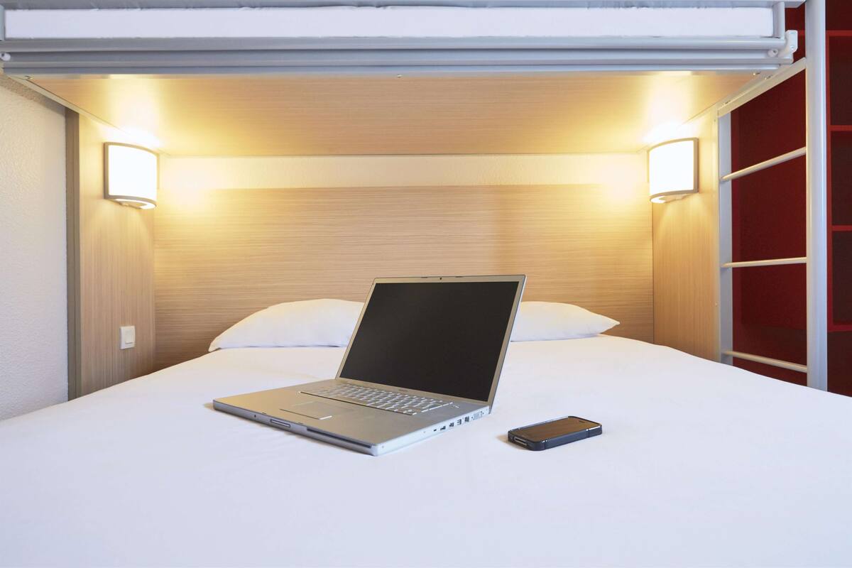A bed with a laptop and a smartphone on it, two wall-mounted lights, and a red wall.