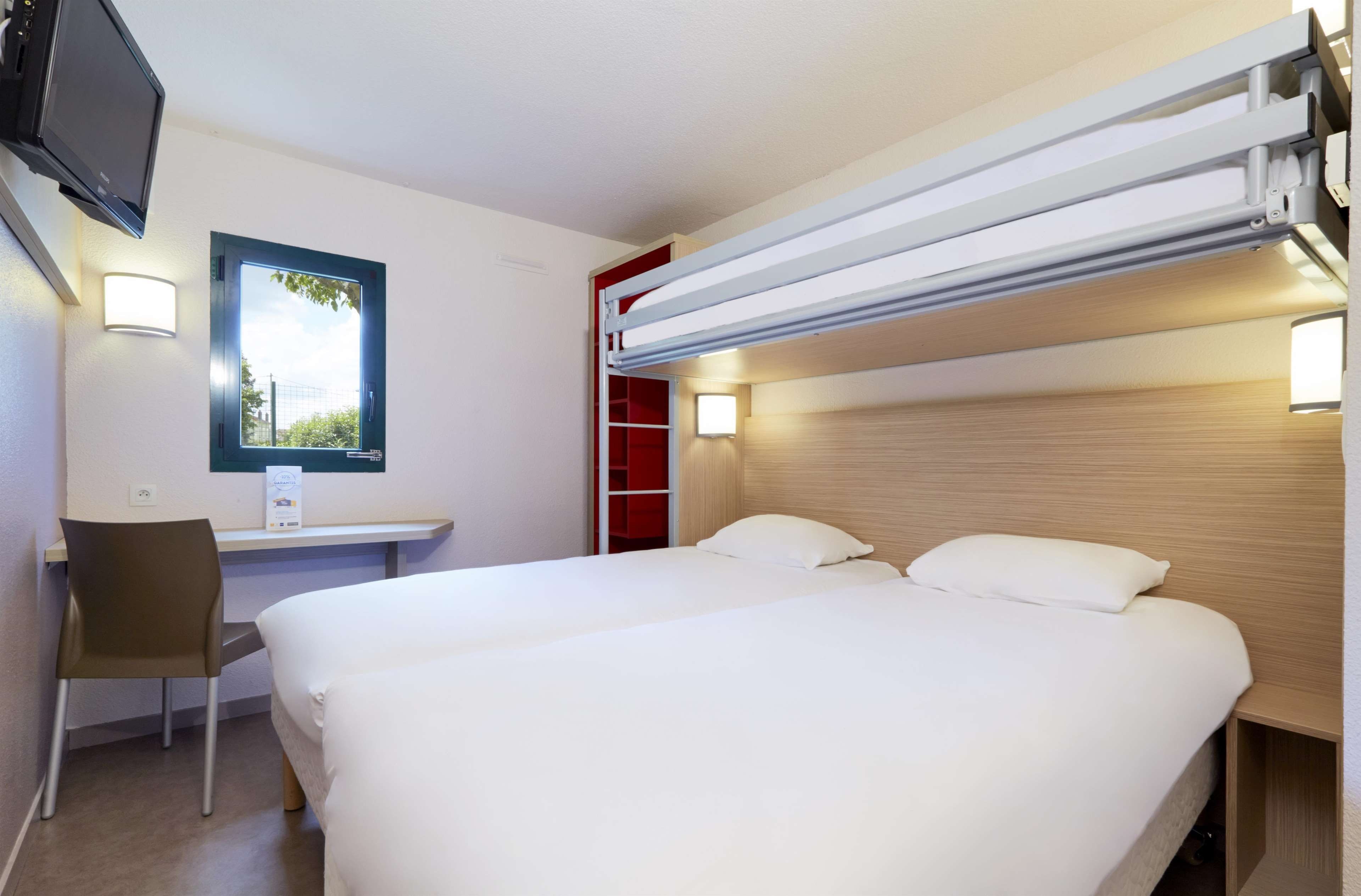 A hotel room with a bed, a desk, a chair, and a TV.