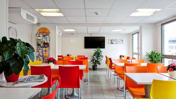 A brightly lit cafeteria with orange and yellow chairs, white tables, and potted plants. - Hotel Première Classe Chalon Sur Saone (Chalon-sur-Saone)