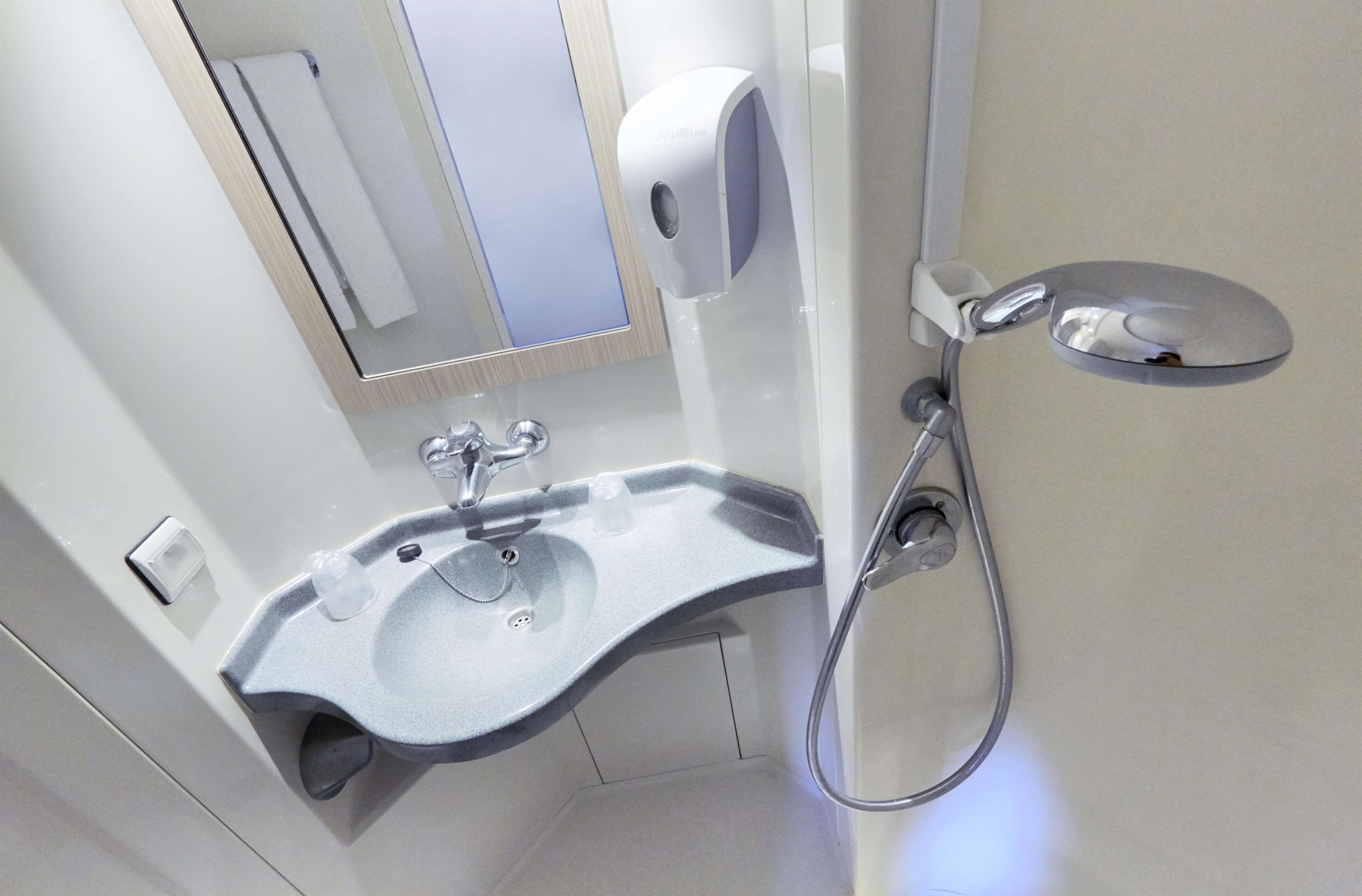 A modern bathroom with a built-in sink, a towel dispenser, and a handheld showerhead.