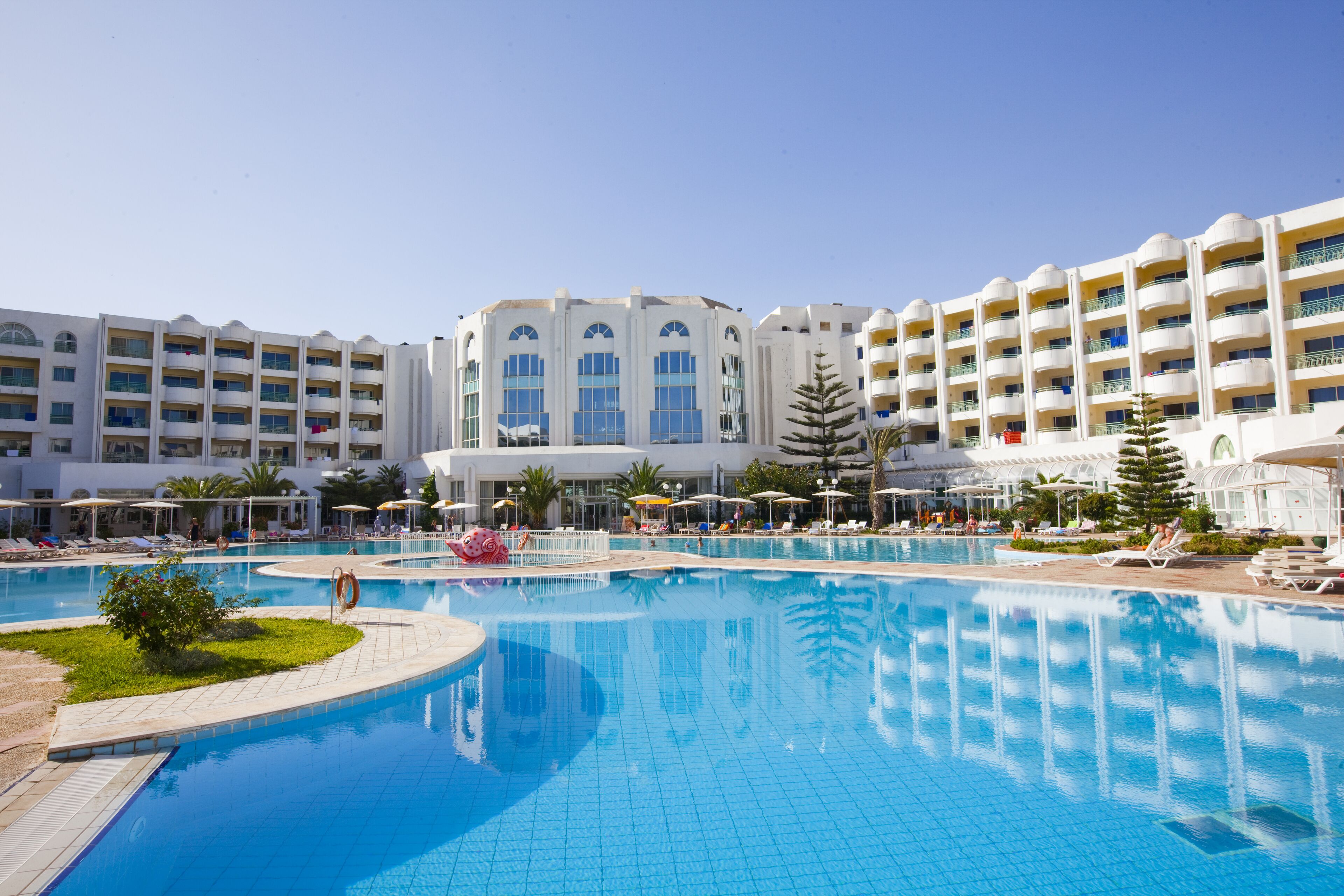 Une grande piscine à l’eau d’un bleu limpide, entourée de chaises longues et de parasols.