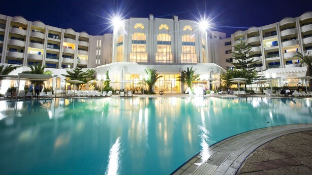 Un hotel con una piscina grande, varios balcones y zonas de estar al aire libre.