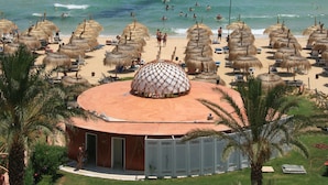 Una playa con sombrillas de paja, una palmera y un edificio con techo abovedado.