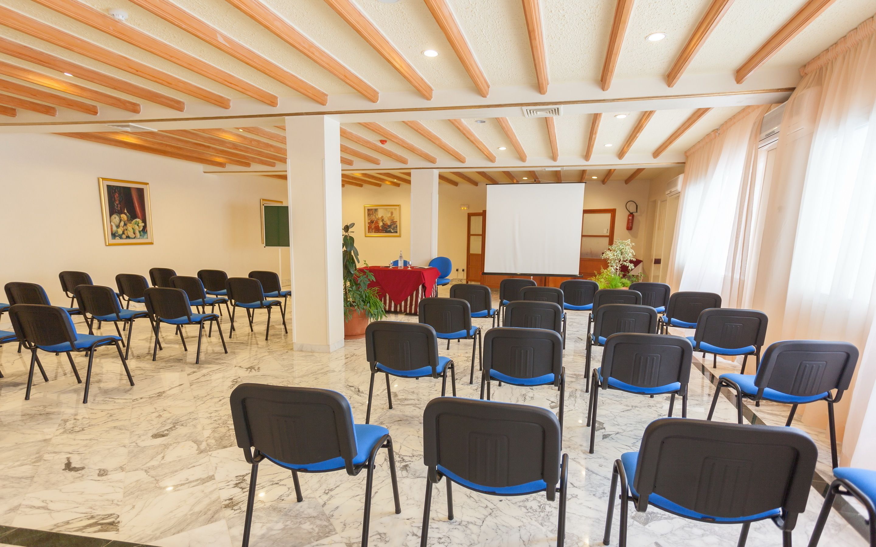 A conference room with rows of chairs, a whiteboard, and a large window with curtains.