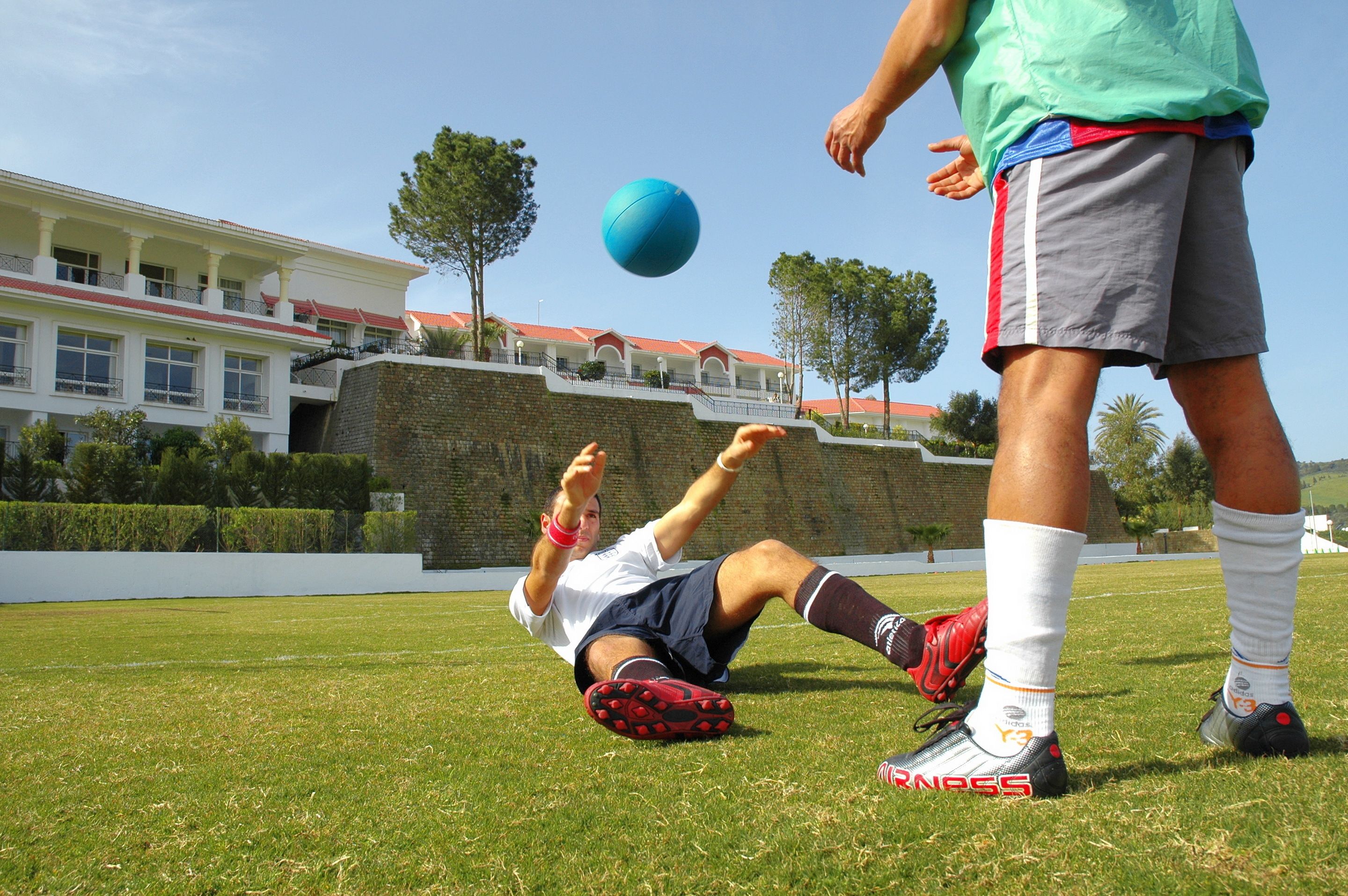 A person playing soccer on a grassy field with a building in the background.