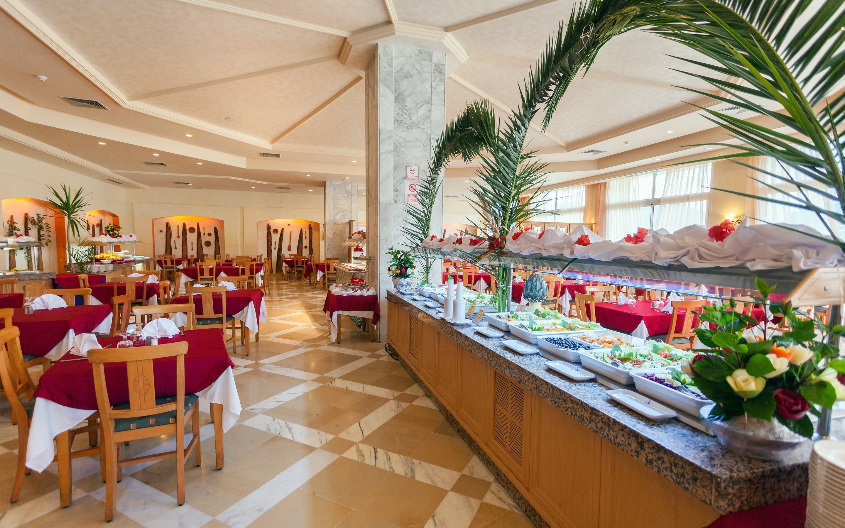 A buffet area with a marble column, wooden tables with red tablecloths, and a variety of food options.