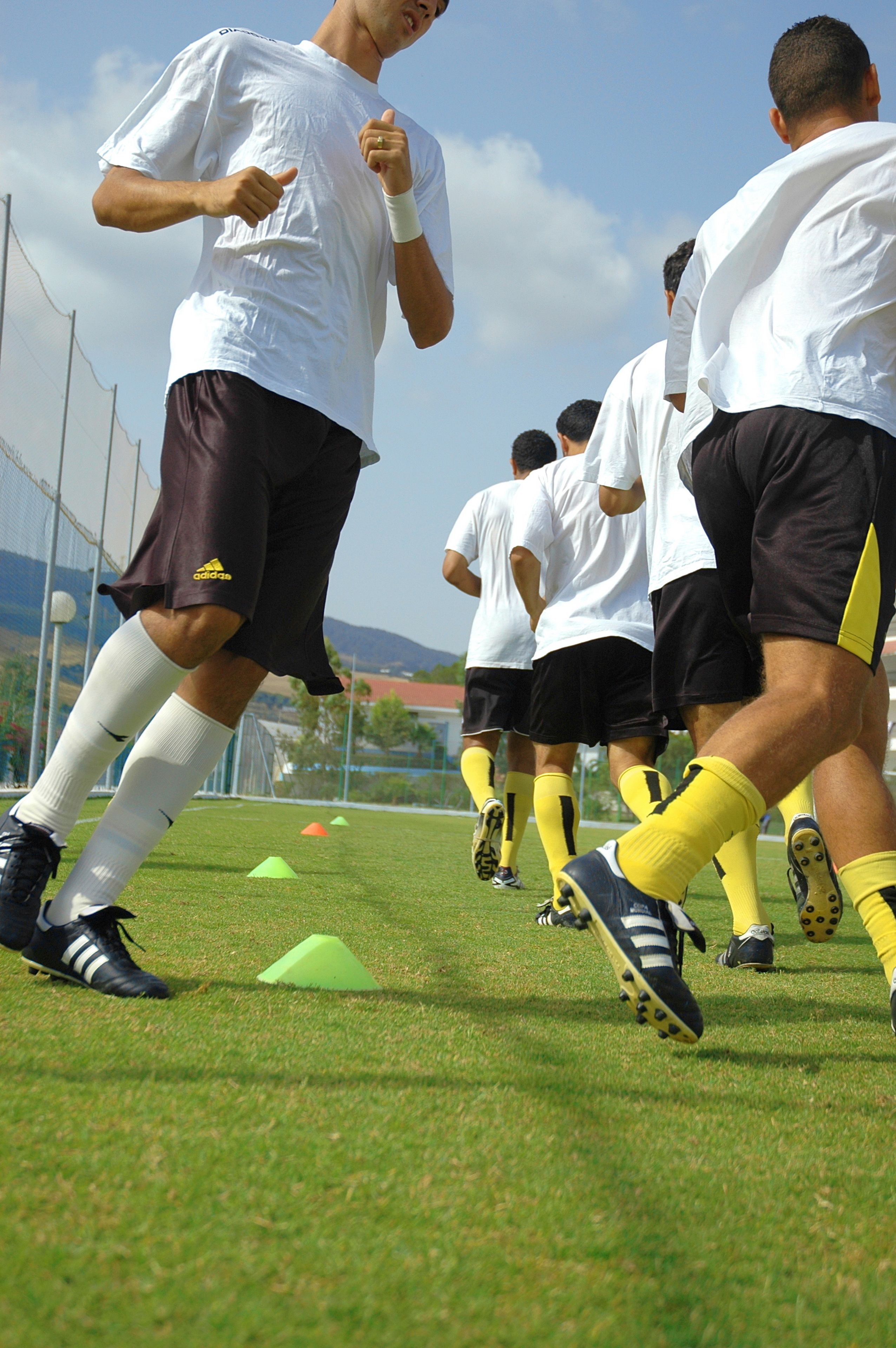 A group of people in sports attire on a grassy field with training cones.